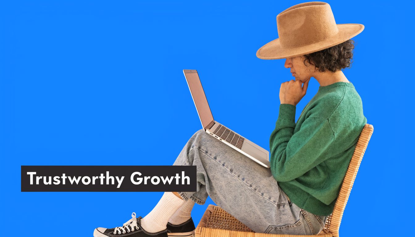 A person in a hat and green sweater sitting on a chair using a laptop computer.
